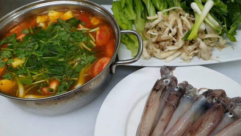 Nồi lẩu mực và đĩa mực tươi cùng rau ăn kèm