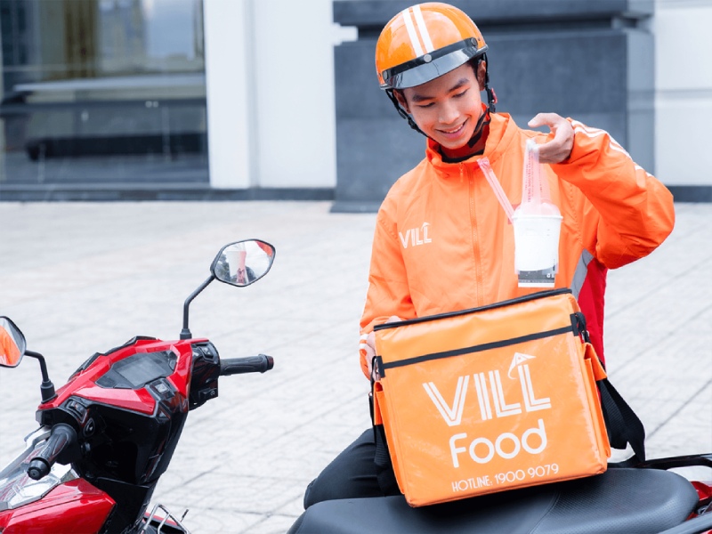 Shipper VIL Food mặc áo cam, cầm ly trà sữa và túi giữ nhiệt