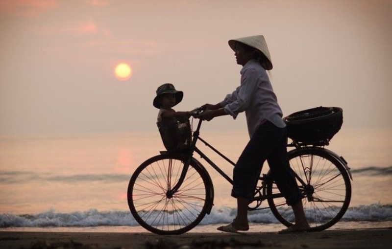 Hình ảnh mẹ đạp xe chở con nhỏ bên bờ biển lúc hoàng hôn