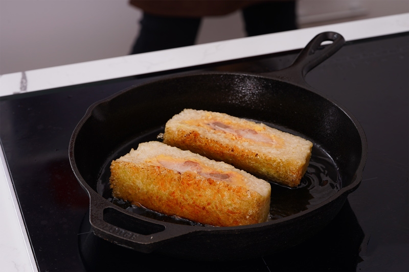 Bánh tét cắt khúc đang được chiên vàng giòn trong chảo gang