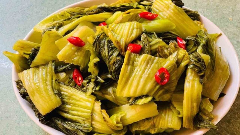 Dưa cải muối giòn vàng với vài lát ớt đỏ trang trí trong tô trắng