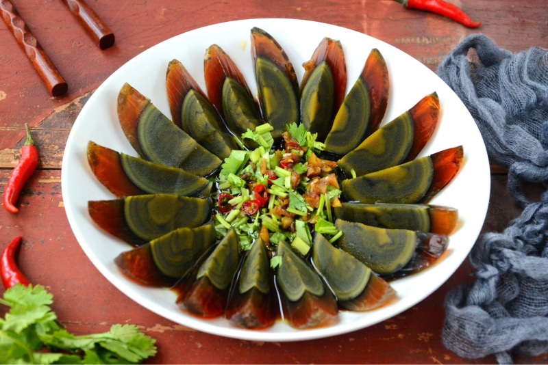 Món trứng bắc thảo cắt lát bày trên đĩa, trang trí hành và ớt