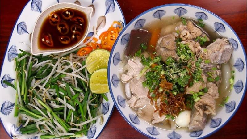 Bánh canh bột lọc nấu xương heo, ăn kèm giá, chanh, nước mắm và rau thơm.