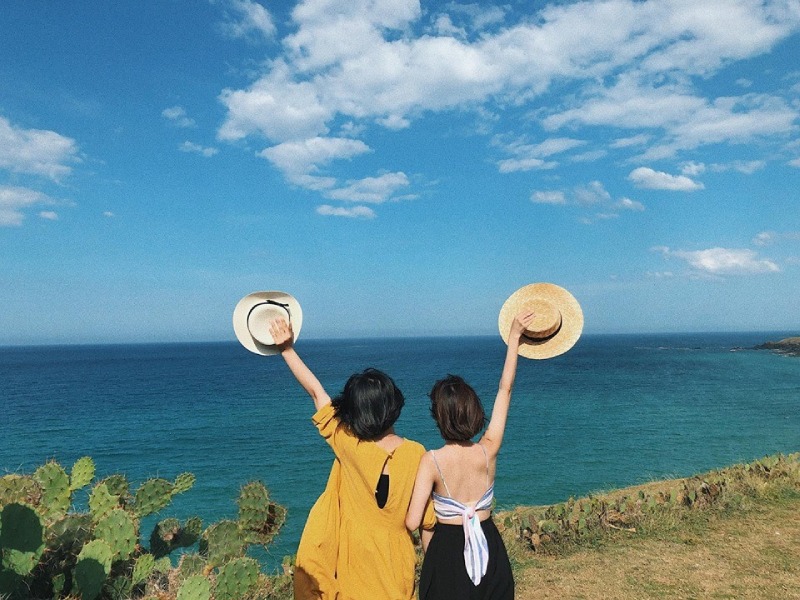 Hai cô gái giơ nón hướng ra biển xanh trong ngày nắng đẹp