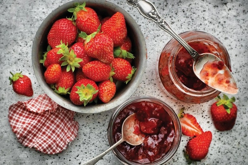 Dâu tây tươi và hũ mứt dâu đặt trên mặt bàn