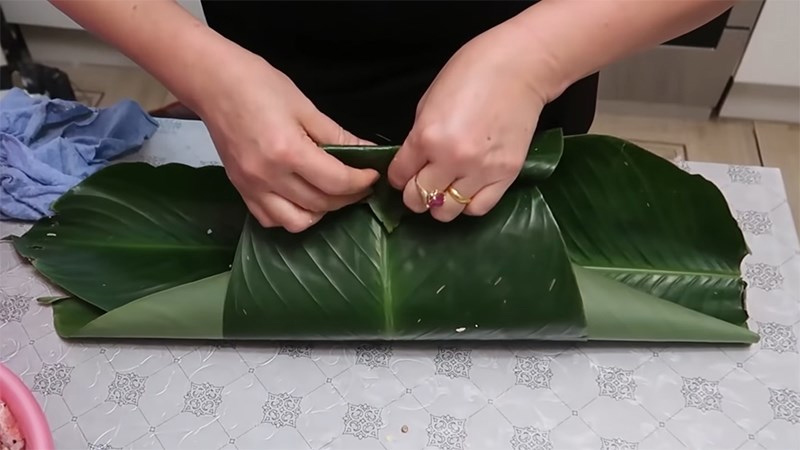 Bỏ nguyên liệu vào nén chặt và túm hai mép lá dong lại sau đó cuộn chặt