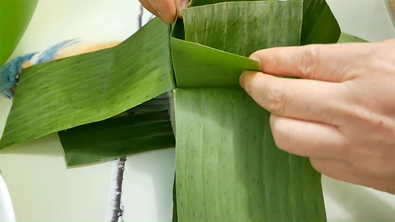 Gấp đôi 4 miếng lá nhỏ lại rồi đặt vào nếp góc của 4 góc hộp