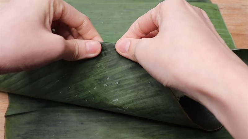 Gấp 2 mép lá chéo vào giữa, giữ nếp gấp và dựng bánh lên