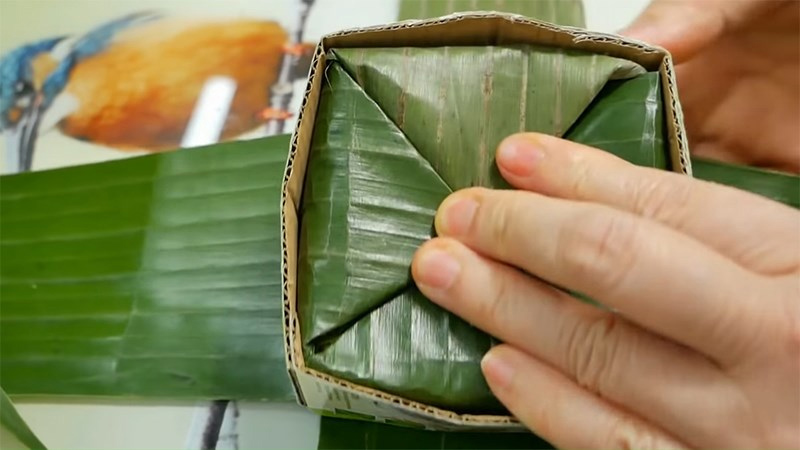 Một tay nhấc hộp carton lên, một tay còn lại giữ bánh